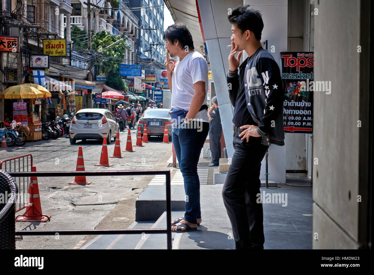 Young Asian men stepping outside of a shopping mall to smoke cigarettes in the accepted smoking area. Thailand Southeast Asia Stock Photo