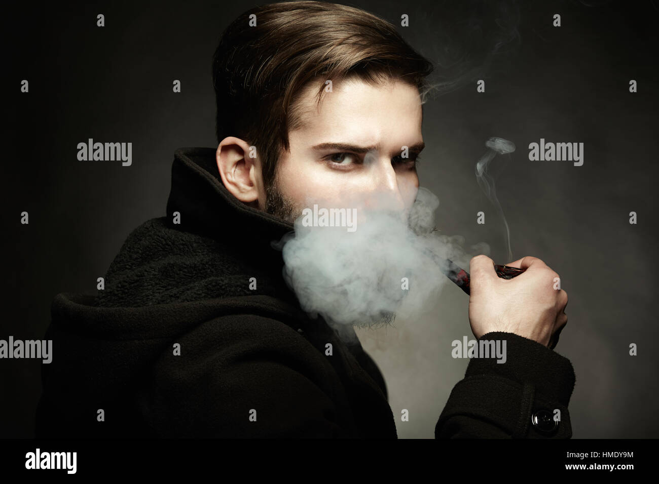 Artistic dark portrait of the young beautiful man. The young man smokes a tube. Close up Stock Photo