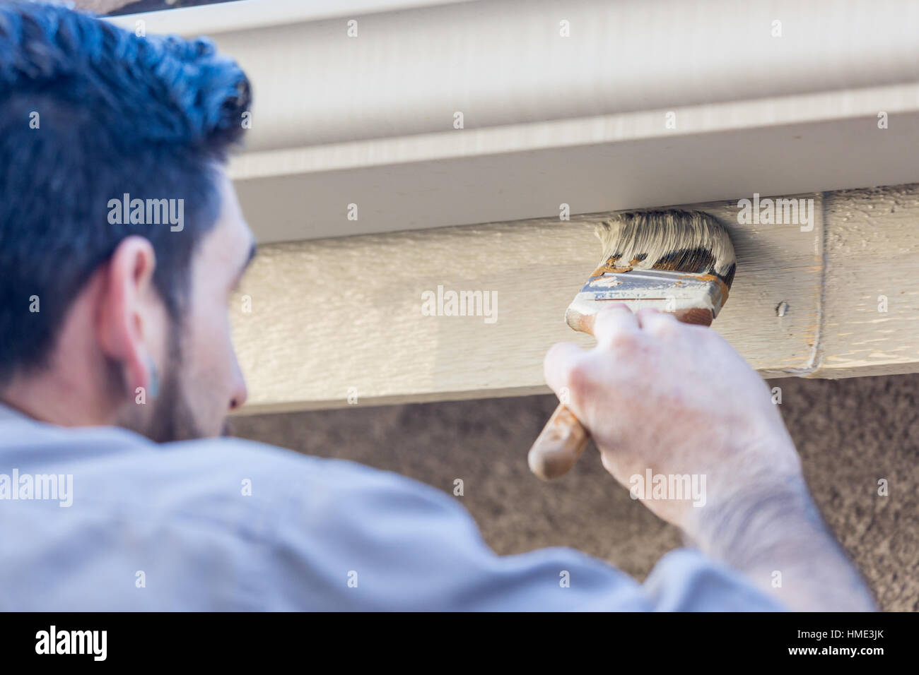 Professional Painter Using A Brush to Paint House Fascia Under Rain