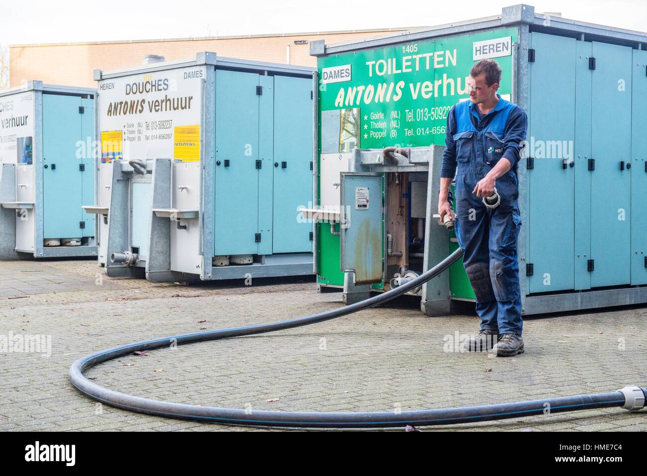 Tilburg, Netherlands. Male employee installing a sewer hose on a few mobile toilets and showers, installed behind an emergancy shelter for refugees. Stock Photo