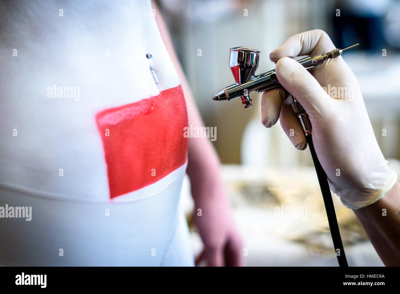 Hand holding air brush in body painting woman body. Paintbrush artist is covering body with white and red paint using a template to make a tatoo. Stock Photo