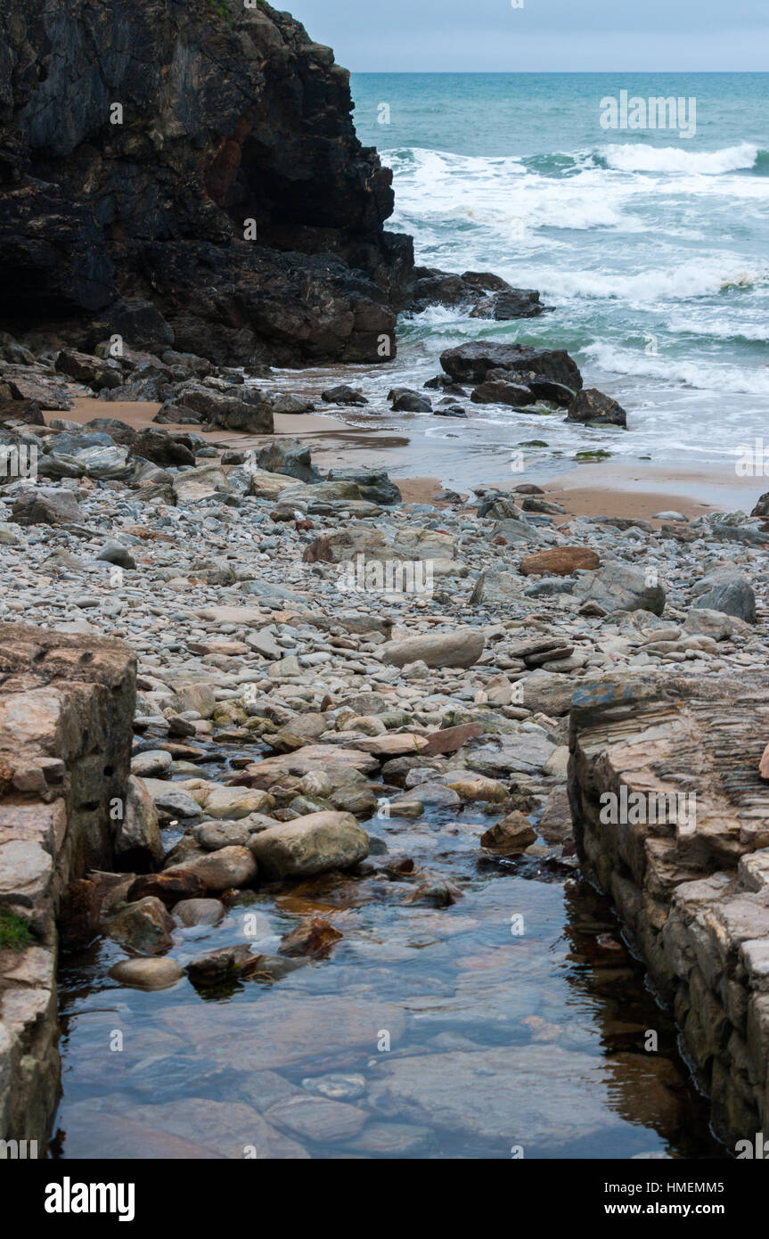 Stream running into the sea through rocks and pebbles at Chapel Porth, St Agnes, Cornwall, alongside Wheal Coates mine. Used to power ore crushers. Stock Photo