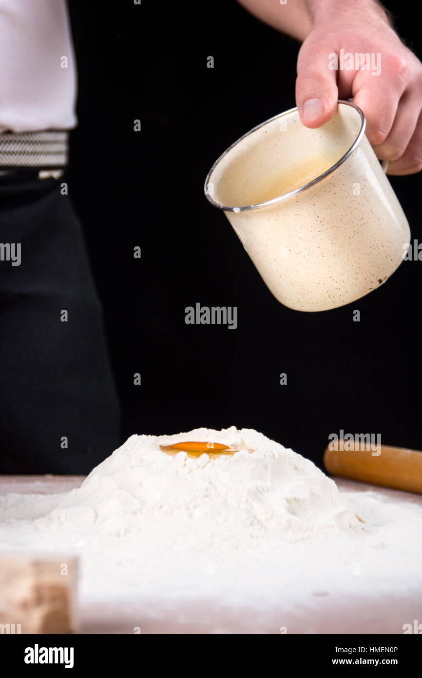 Man pouring milk and yeast on flour. Making pastry Stock Photo