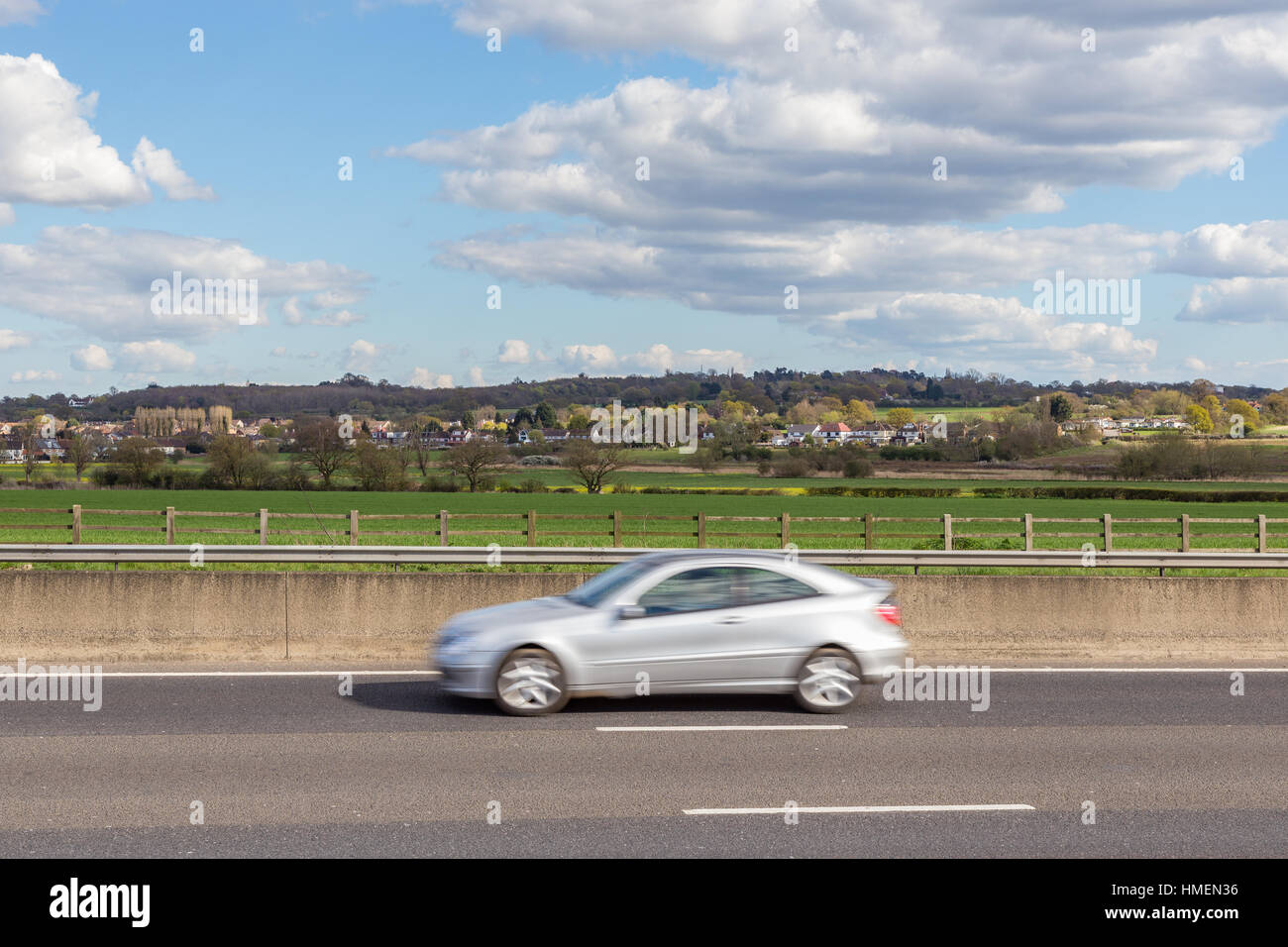 Speeding car on the motorway with countryside and village in the background. Stock Photo