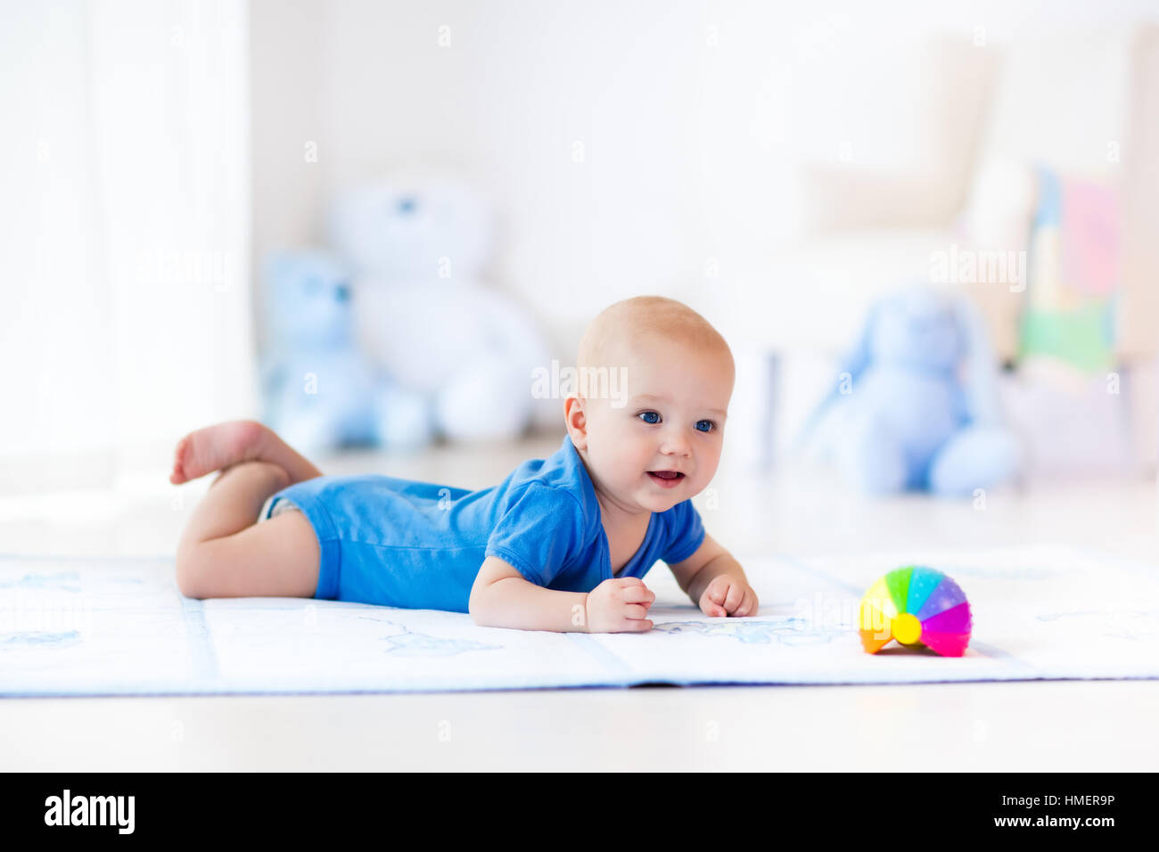 Cute baby boy on colorful playmat and gym, playing with hanging rattle toys. Kids activity and play center for early development Stock Photo