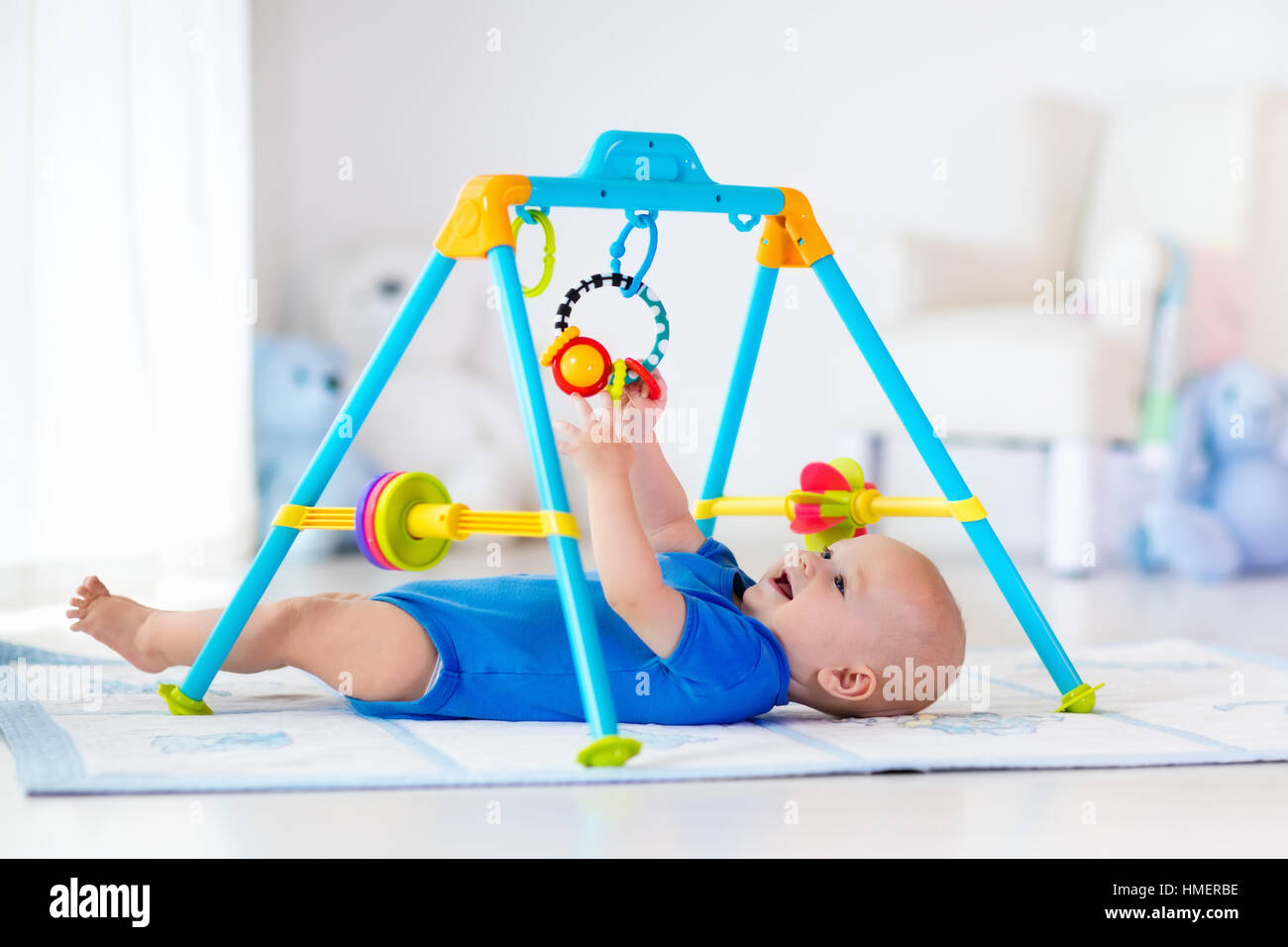 Cute baby boy on colorful playmat and gym, playing with hanging rattle toys. Kids activity and play center for early development Stock Photo