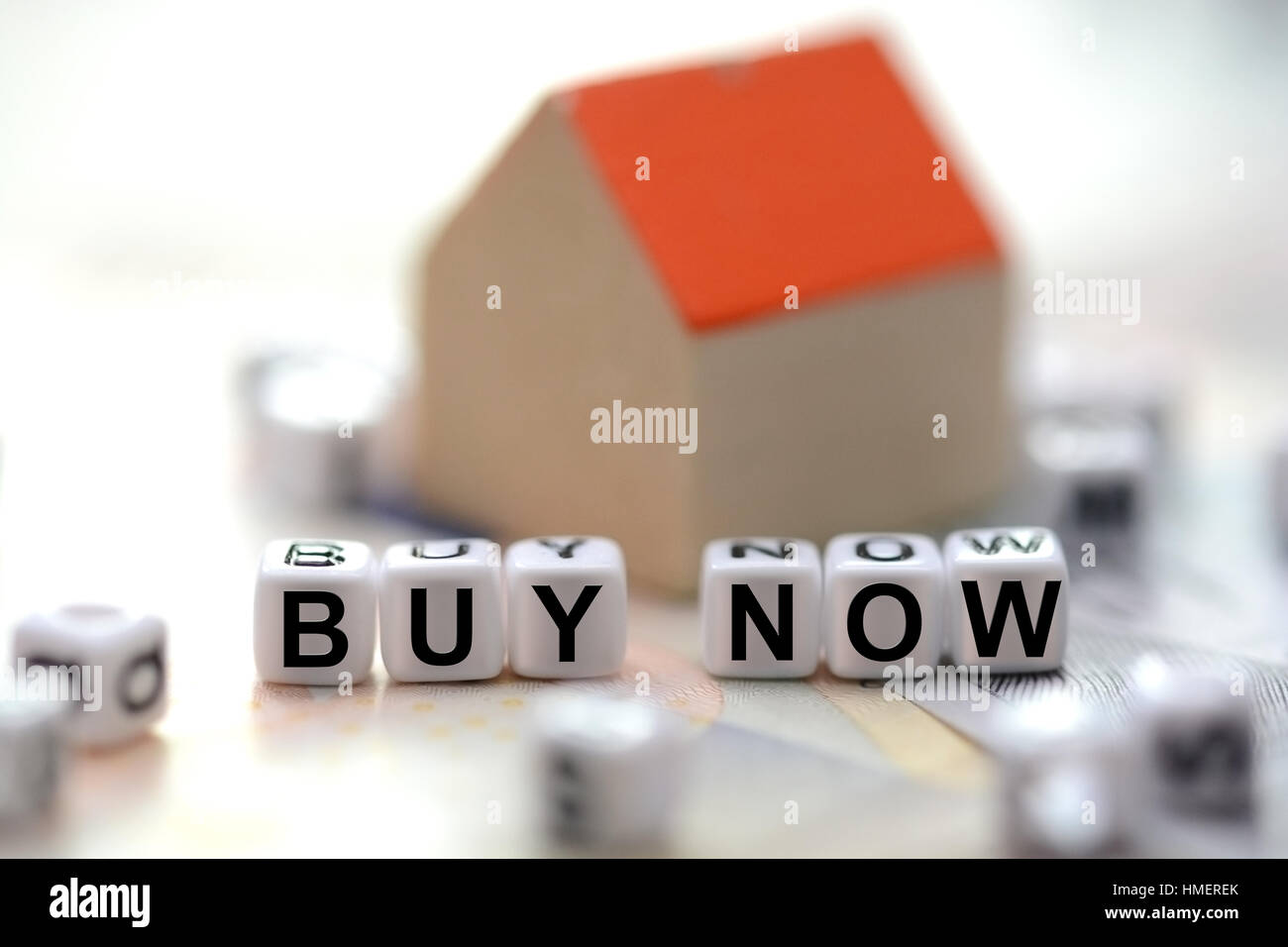 Buy now text spelled with tiled letter beads and a blurred small model house in the background Stock Photo