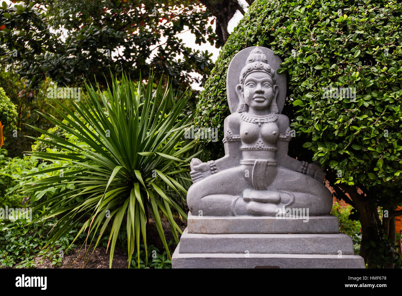 Statue of Buddha on stone platform in temple surrounded by green trees Stock Photo
