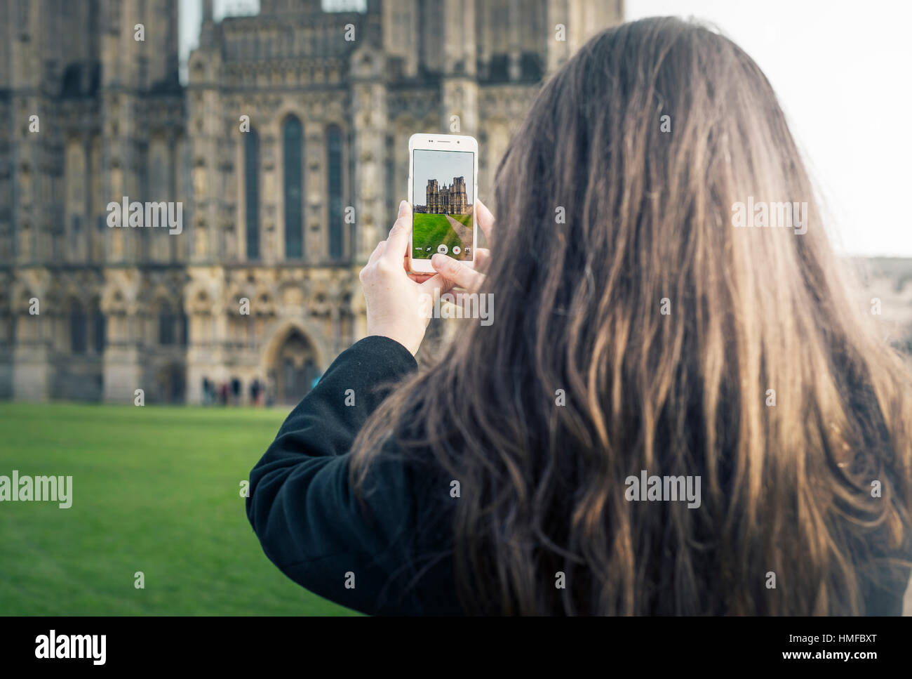 A woman taking a picture of Wells cathedral on a mobile phone Stock Photo