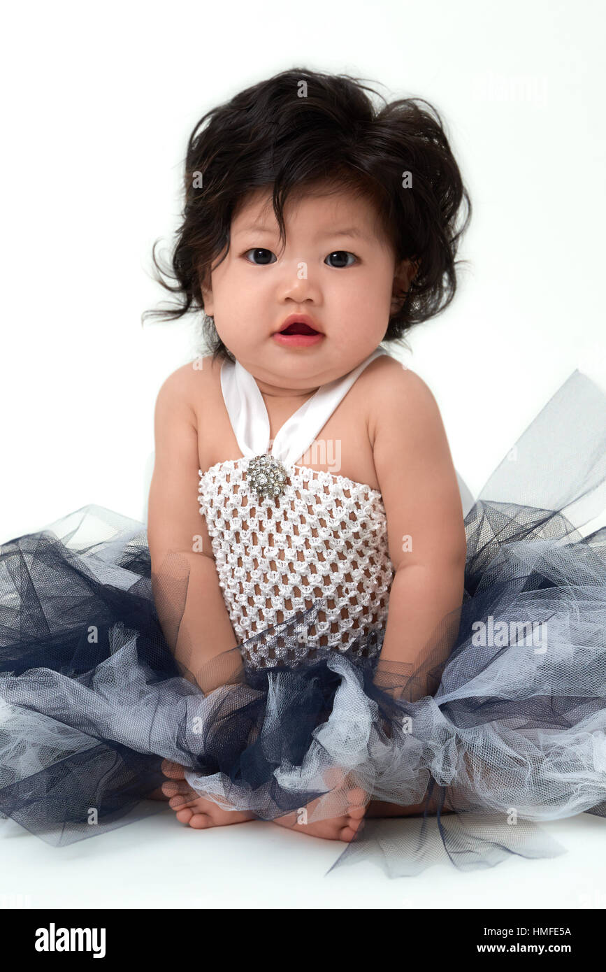 Cute Asian baby girl in flare dress sitting up. Stock Photo