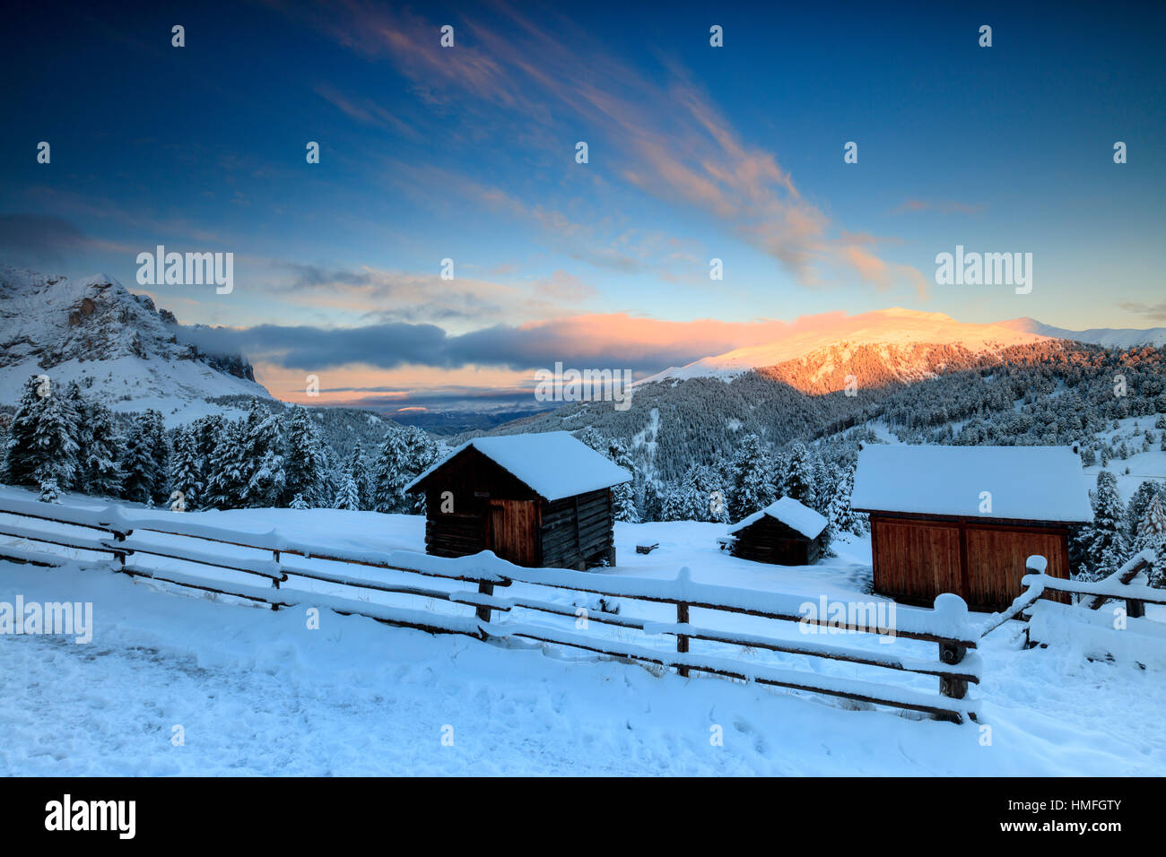 The sunrise lights up the snowy woods and huts, Passo Delle Erbe, Funes Valley, South Tyrol, Italy Stock Photo