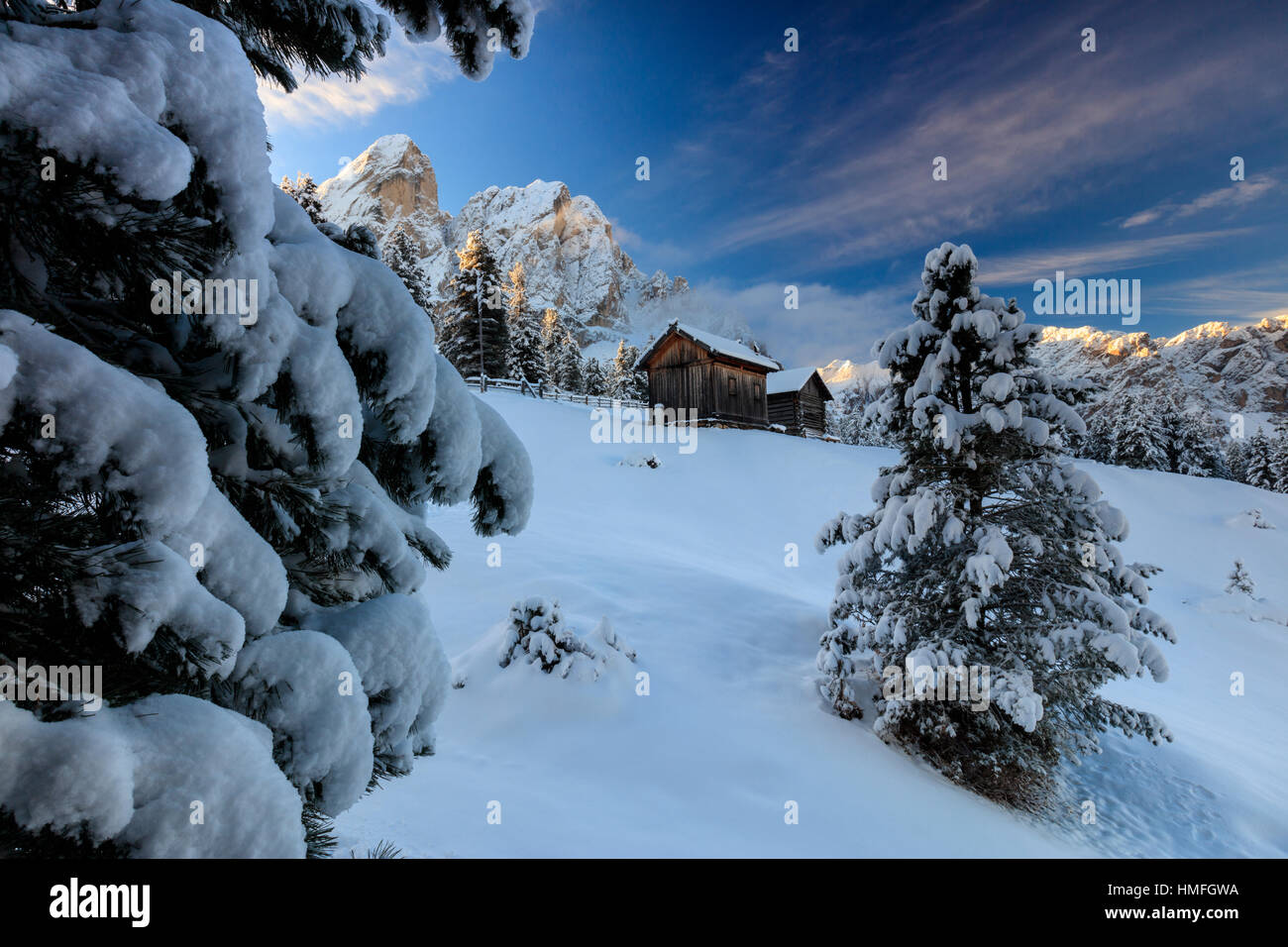 The snowy peak of Sass De Putia frames the wooden hut and woods at dawn, Passo Delle Erbe, Funes Valley, South Tyrol, Italy Stock Photo
