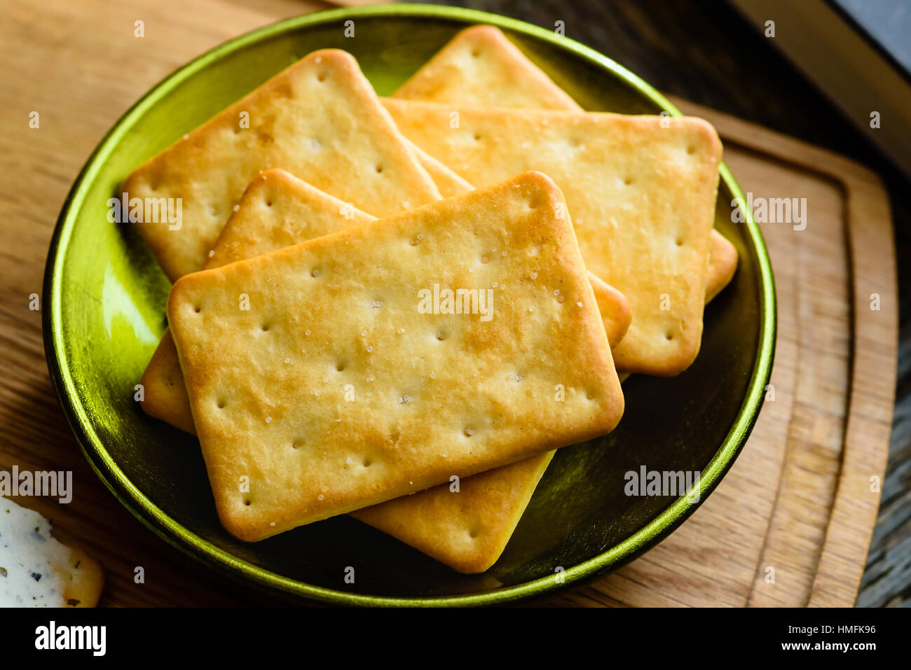 Salted crackers in green bowl on wooden tray. Part of book visible in