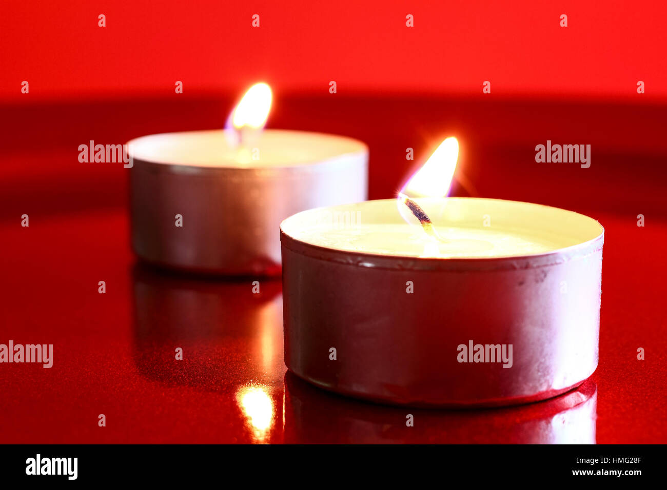 Two burning wax tea candles isolated on a red shiny surface Stock Photo