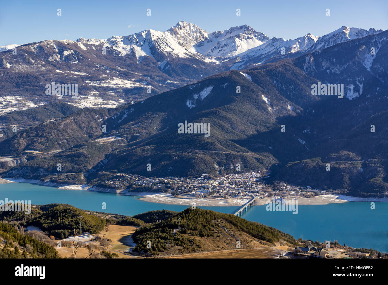 Elevated view over Savines-le-Lac Village and Serre Poncon lake in winter. In the distance the Montagnette and Pouzenc mountain peaks. Alps, France Stock Photo