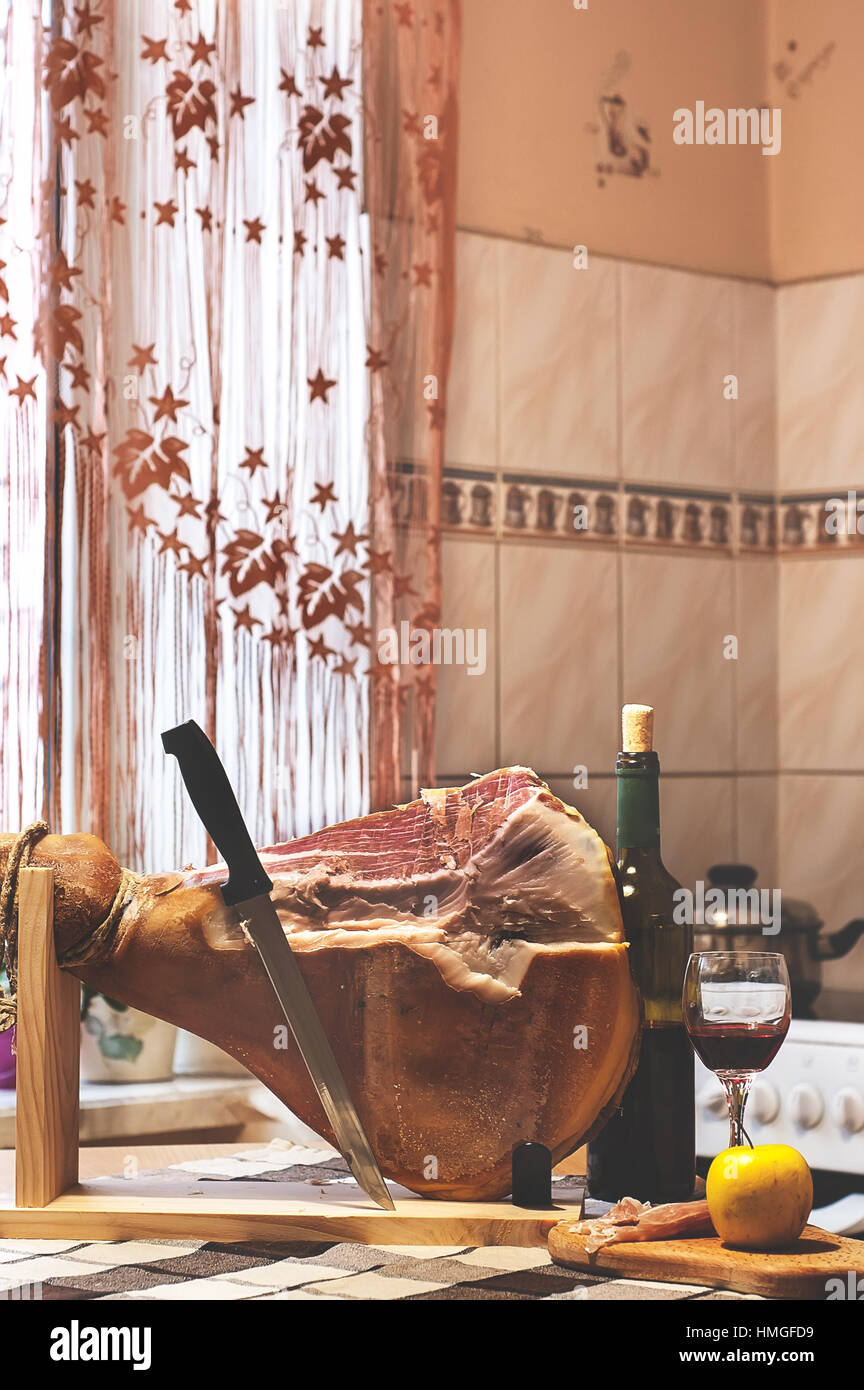 Spanish Jamon Serrano on wooden tabla jamonera with knife, apple, glass and bottle of red wine. Home cooking, food photo concept Stock Photo