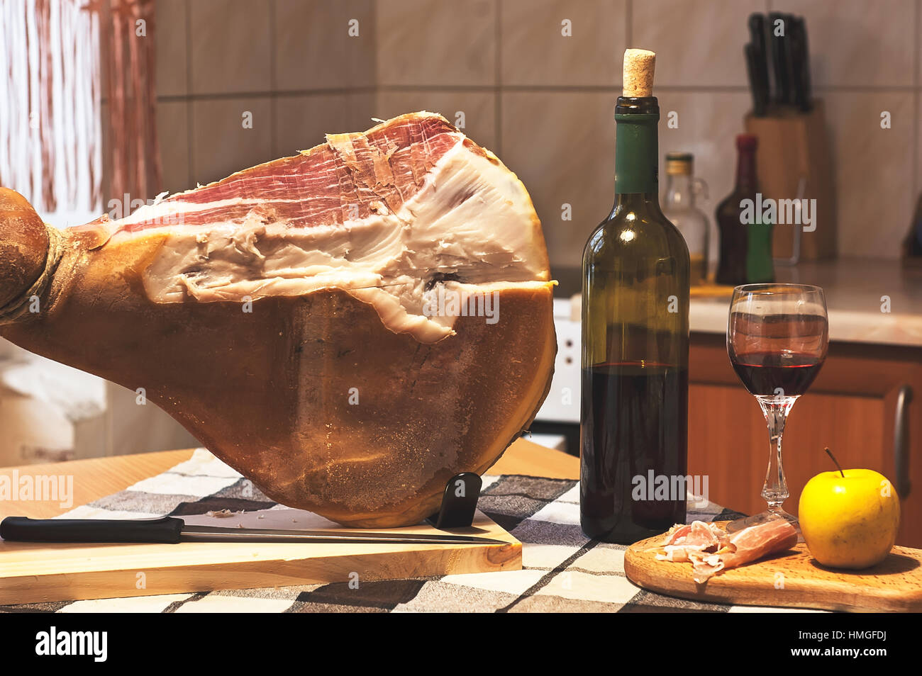 Spanish Jamon Serrano on wooden tabla jamonera with knife, apple, glass and bottle of red wine. Home cooking, food photo concept Stock Photo