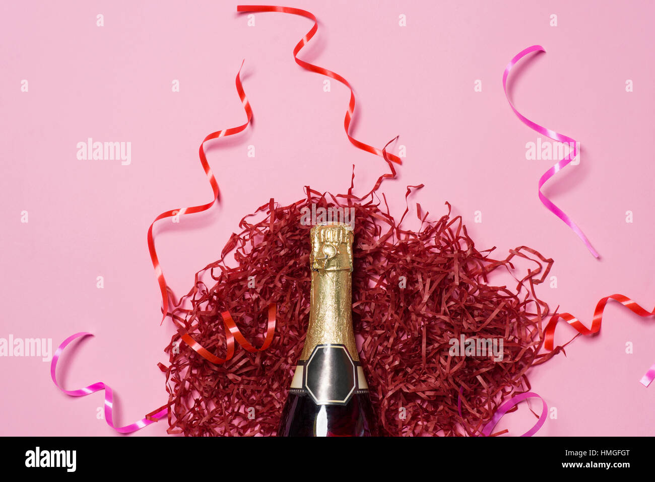 Flat lay of Celebration. Champagne bottle with colorful party streamers on pink background. Stock Photo