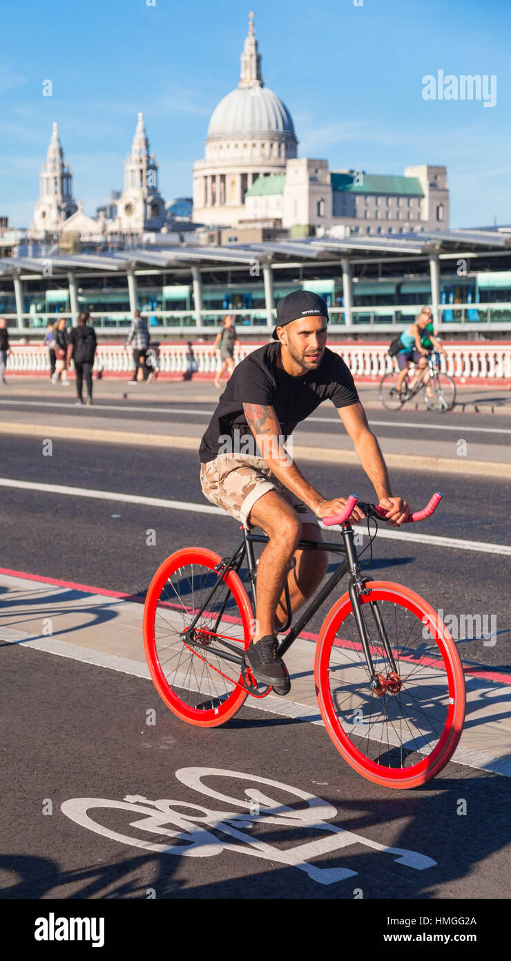 tanned young man riding red wheeled fixie bike on north-south cycle superhighway: Blackfriars bridge, London, with St Pauls in background, summer day Stock Photo