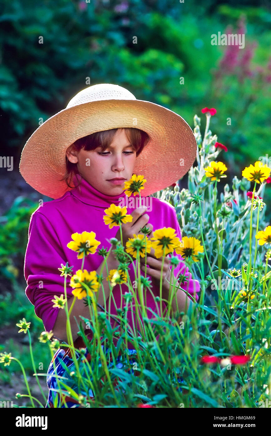 Young girl in a straw hat picking flowers. Stock Photo