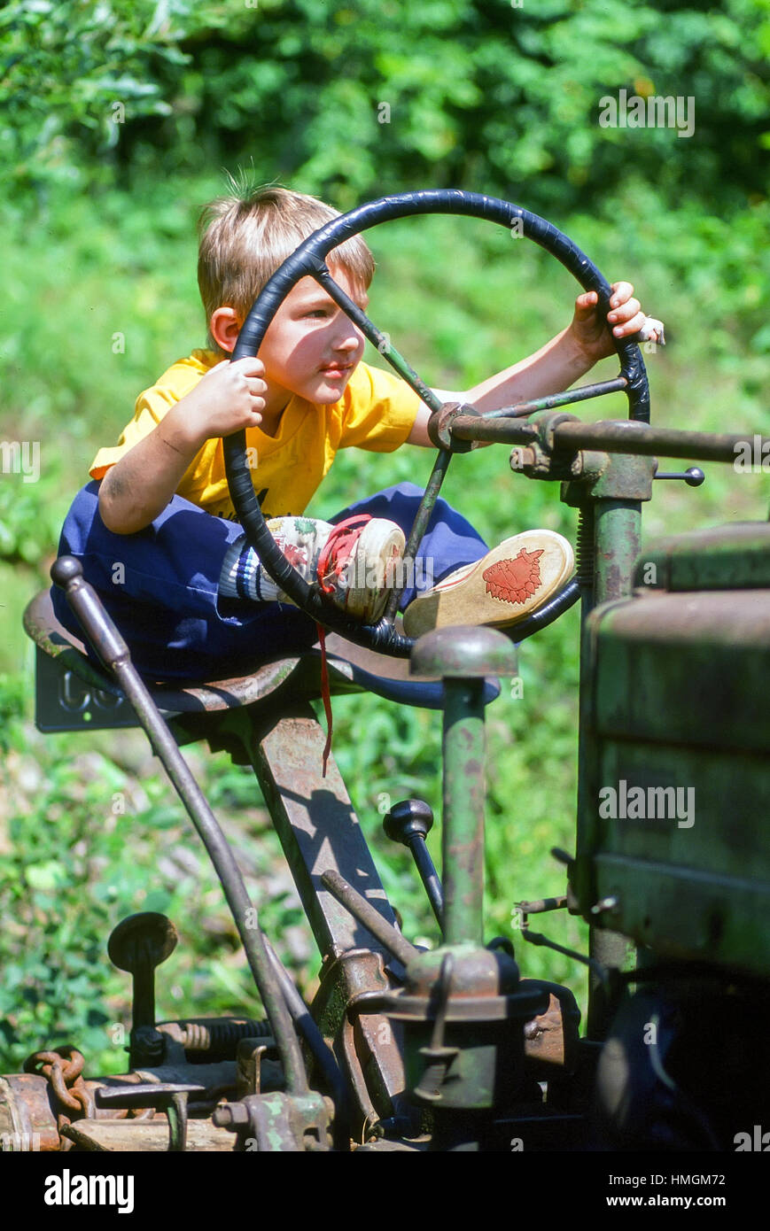 A four year old boy sits behind the wheel of an antique tractor pretend driving on the farm in Ryegate, Vermont, United States. Stock Photo