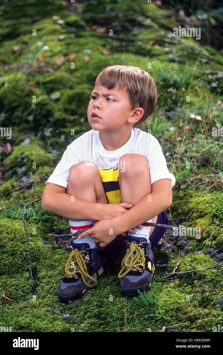 A five year old boy sits on a mossy hill lost in thought with a pensive look on his face in Plainfield, New Hampshire, United States. Stock Photo