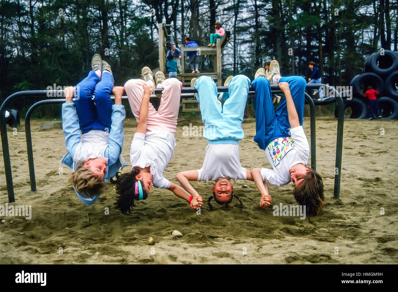 Four happy girl children hanging upside down in a school playground. Stock Photo