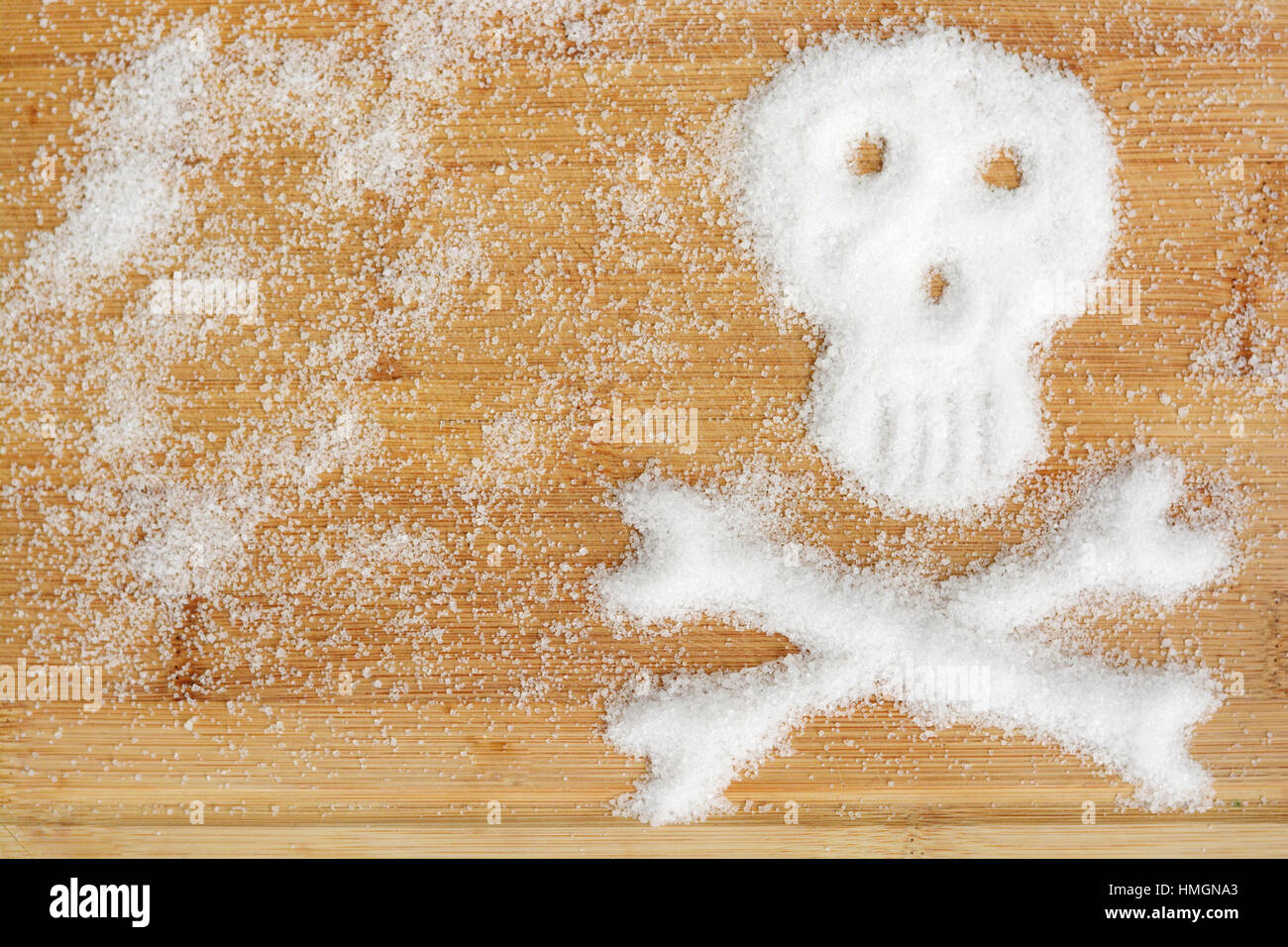 Deadly sugar addiction suggested by spilled white sugar crystals forming a skull on a wooden table Stock Photo