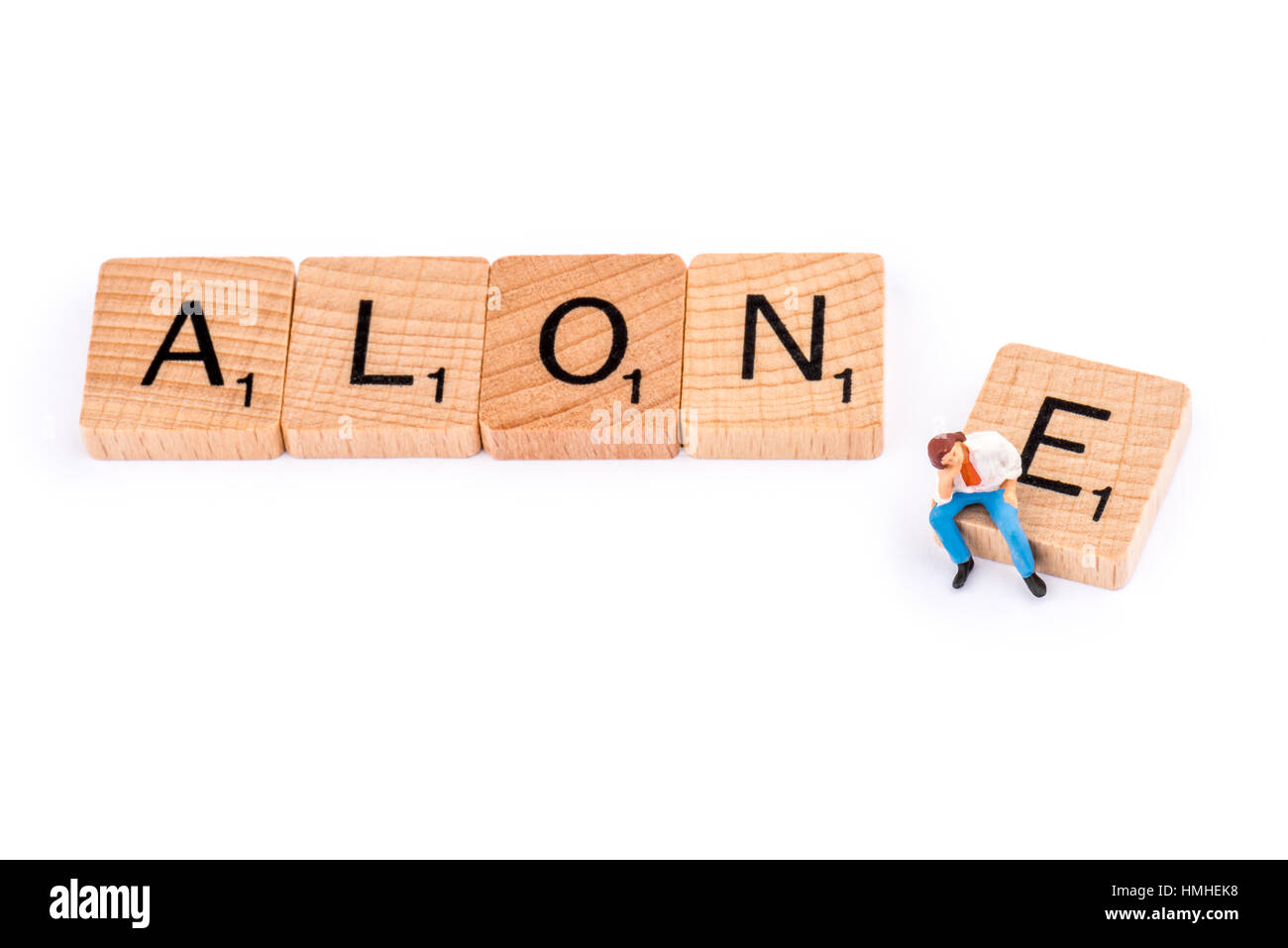 Scrabble letters make up the word ALONE. A young man sits on the letter E of the word ALONE. Stock Photo