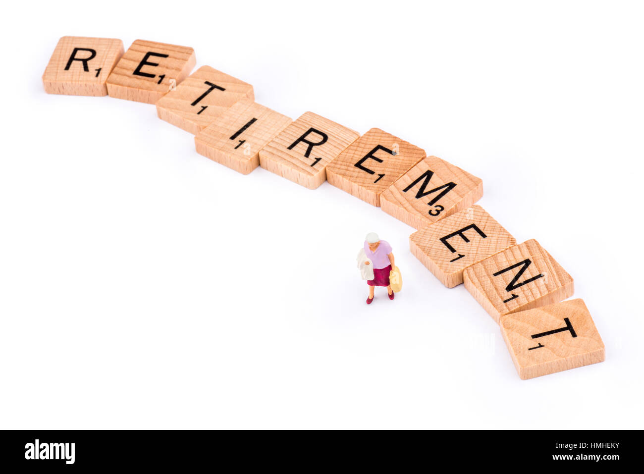 Scrabble letters make up the word RETIREMENT. An elderly lady walks away from the letter E. Stock Photo