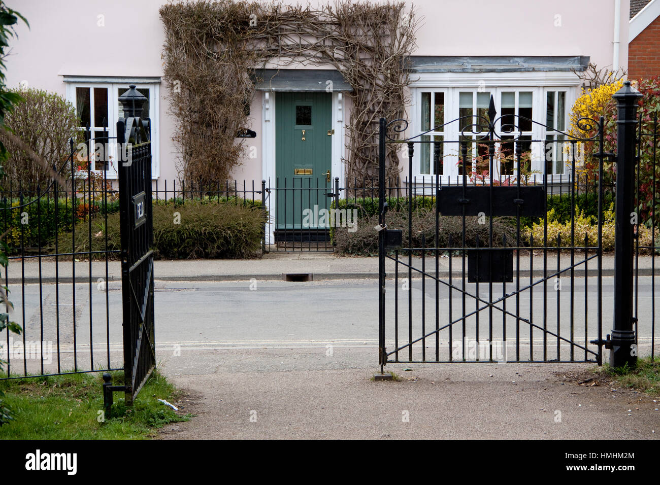 House with climber round the door seen through black metal park gates Stock Photo