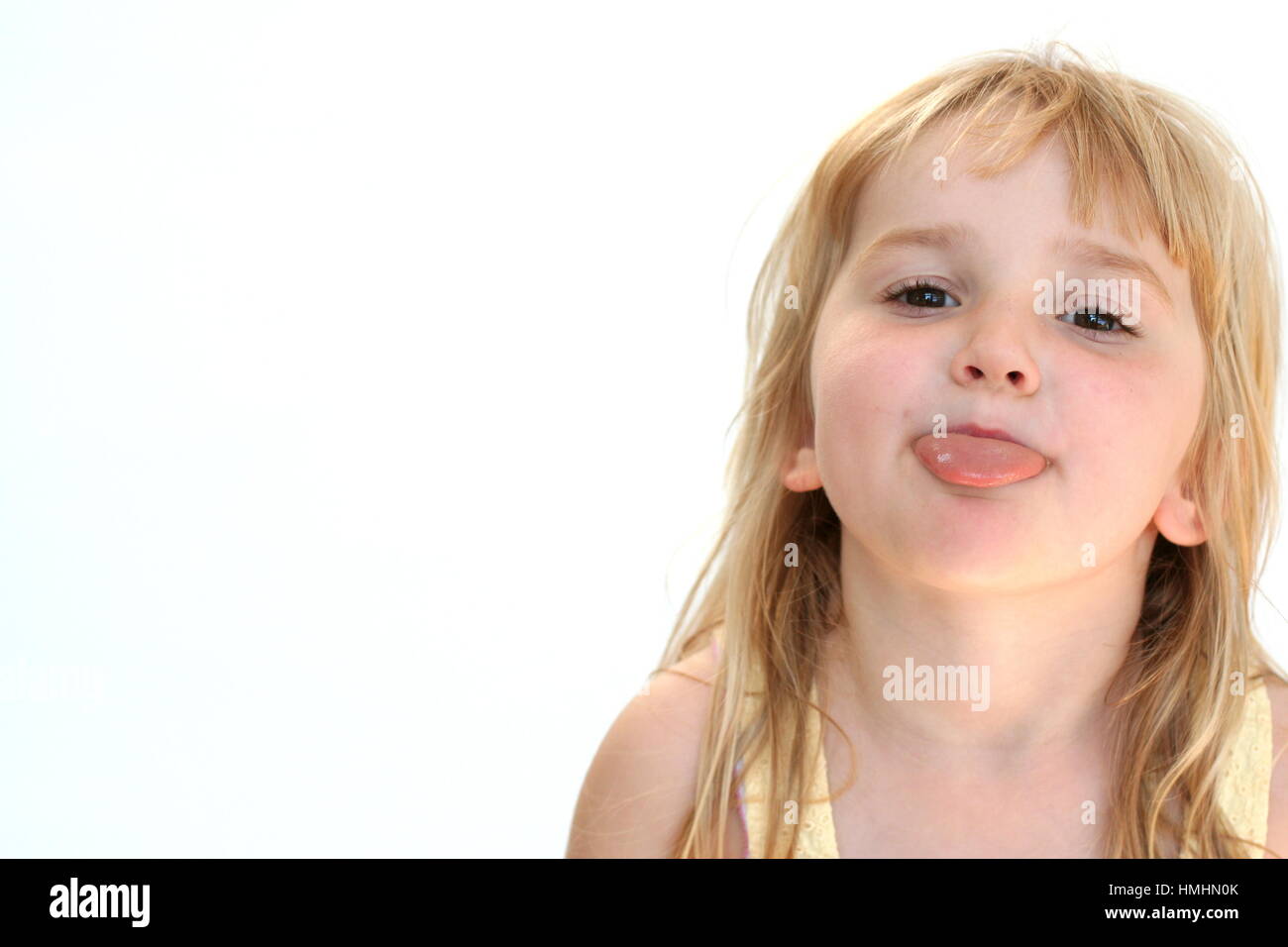 young girl kid blonde child making a funny face sticking tongue out having fun Stock Photo