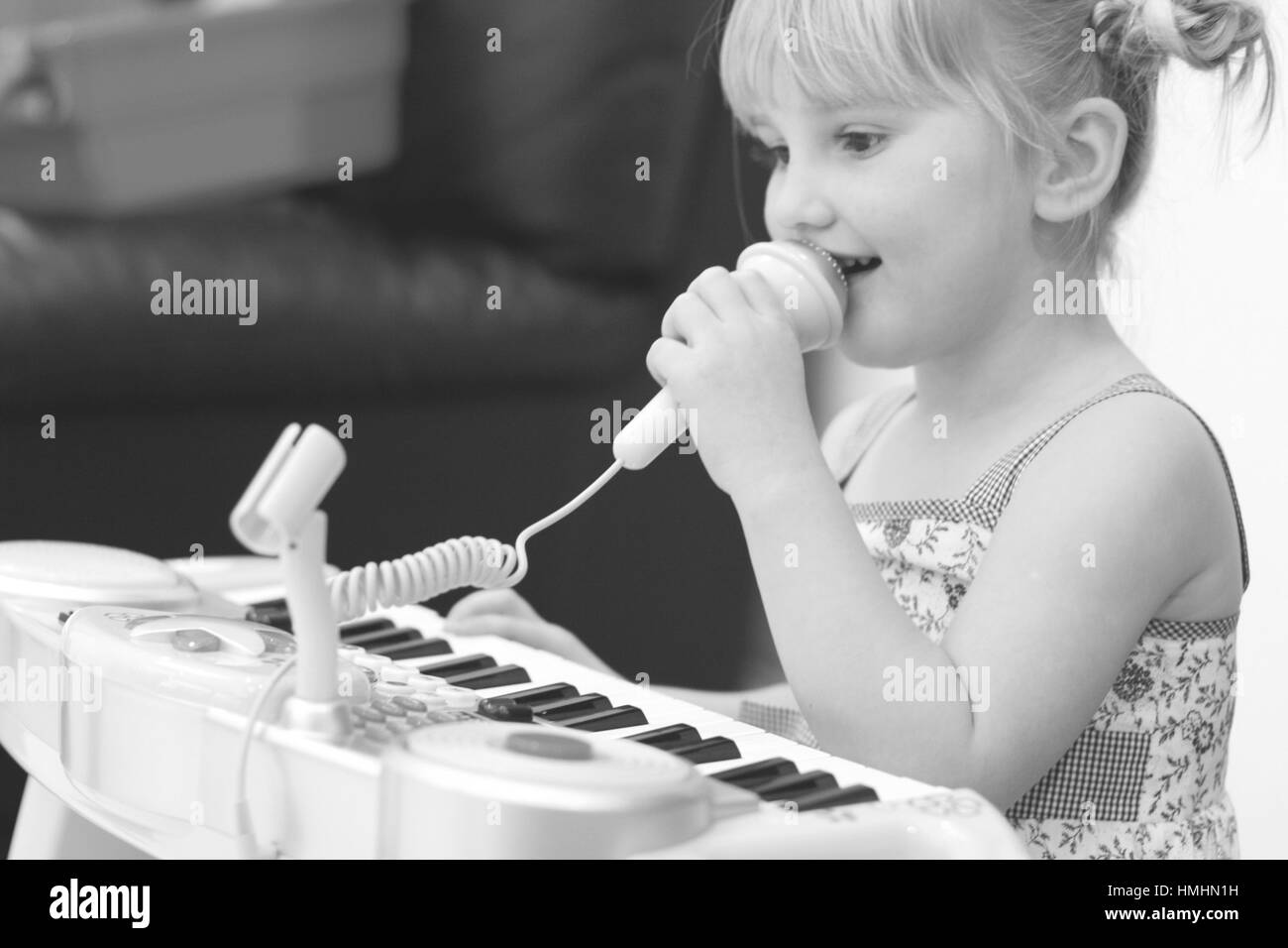 Little girl child kid holding a microphone mouth singing playing toy keyboard, piano, pigtails music lessons, learning, kids playing happiness concept Stock Photo