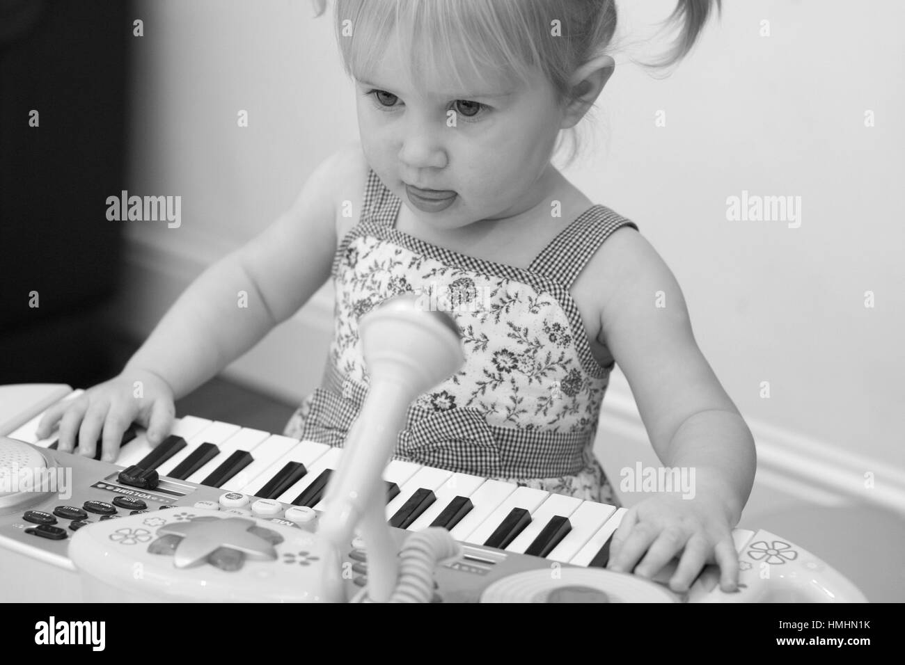 Little  blonde girl child kid playing on the keyboard, piano serious, three year old learning music singing play lessons fun family concept Stock Photo