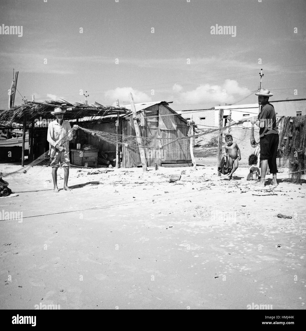 Fischer mit Fischernetz und kleiner Junge am Ufer der Isla Margarita, Venezuela 1966. Fisherman with flue an little boy at the coast of the Isla Margarita, Venezuela 1966. Stock Photo