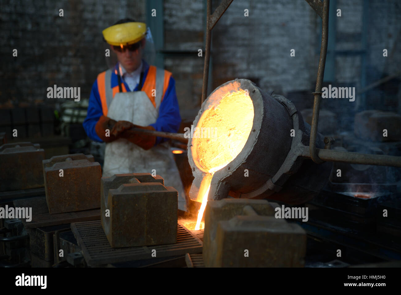 Foundrymen pour molten iron into moulds for making fire grates. (Shot in available light with shallow depth of field.) Stock Photo