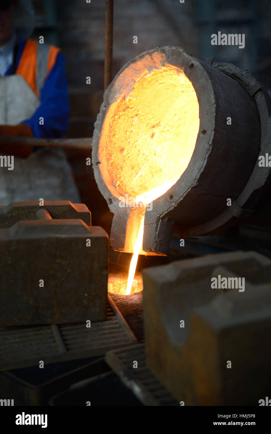 Foundrymen pour molten iron into moulds for making fire grates. (Shot in available light with shallow depth of field.) Stock Photo