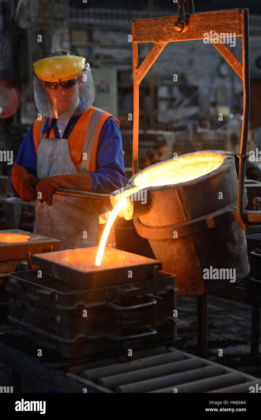 Foundrymen pour molten iron into moulds for making fire grates at a small foundry. (Shot in available light with shallow depth of field.) Stock Photo