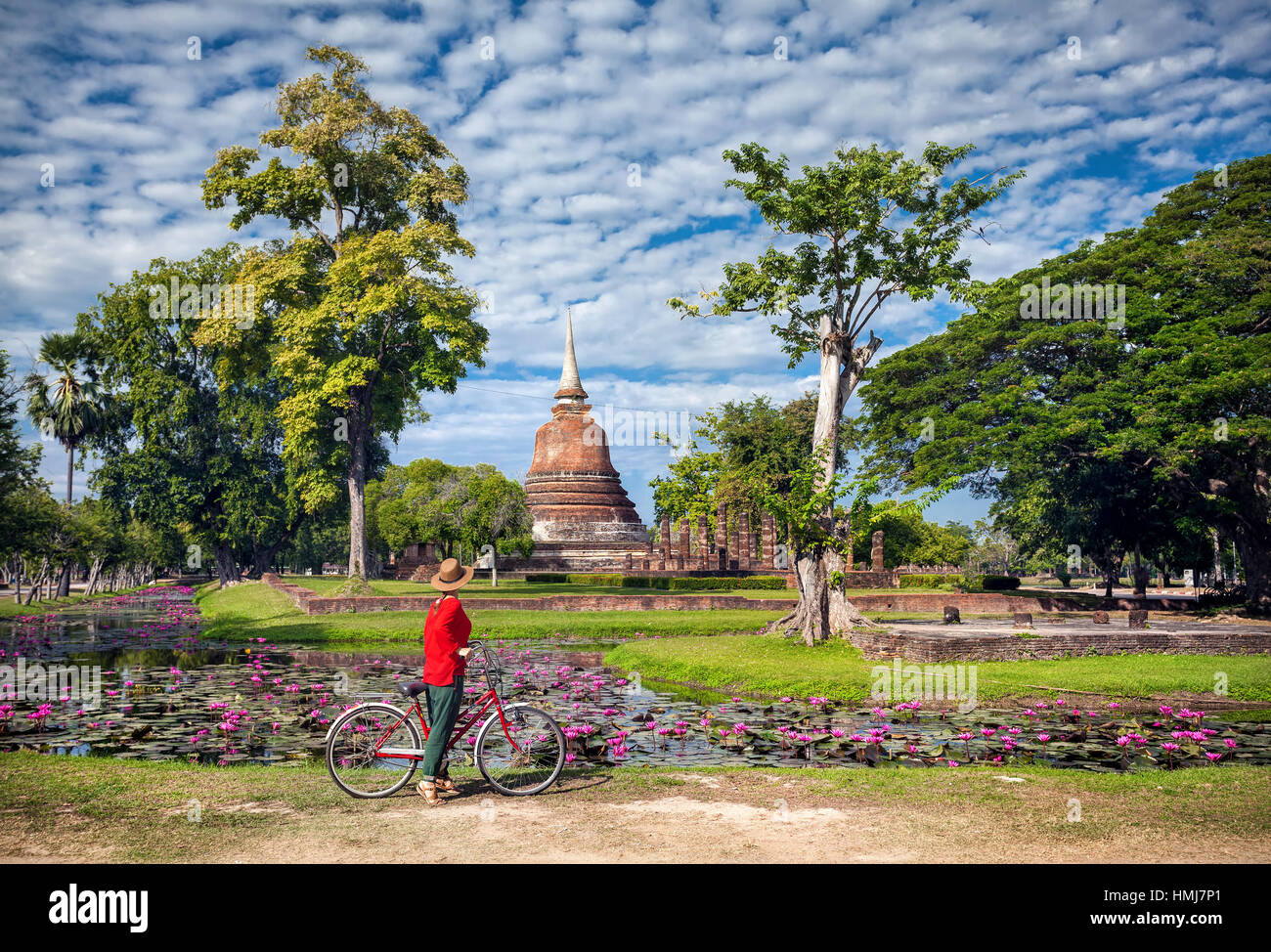 Woman in red shirt riding bicycle near old Buddhist temple in Sukhothai historical park, Thailand Stock Photo