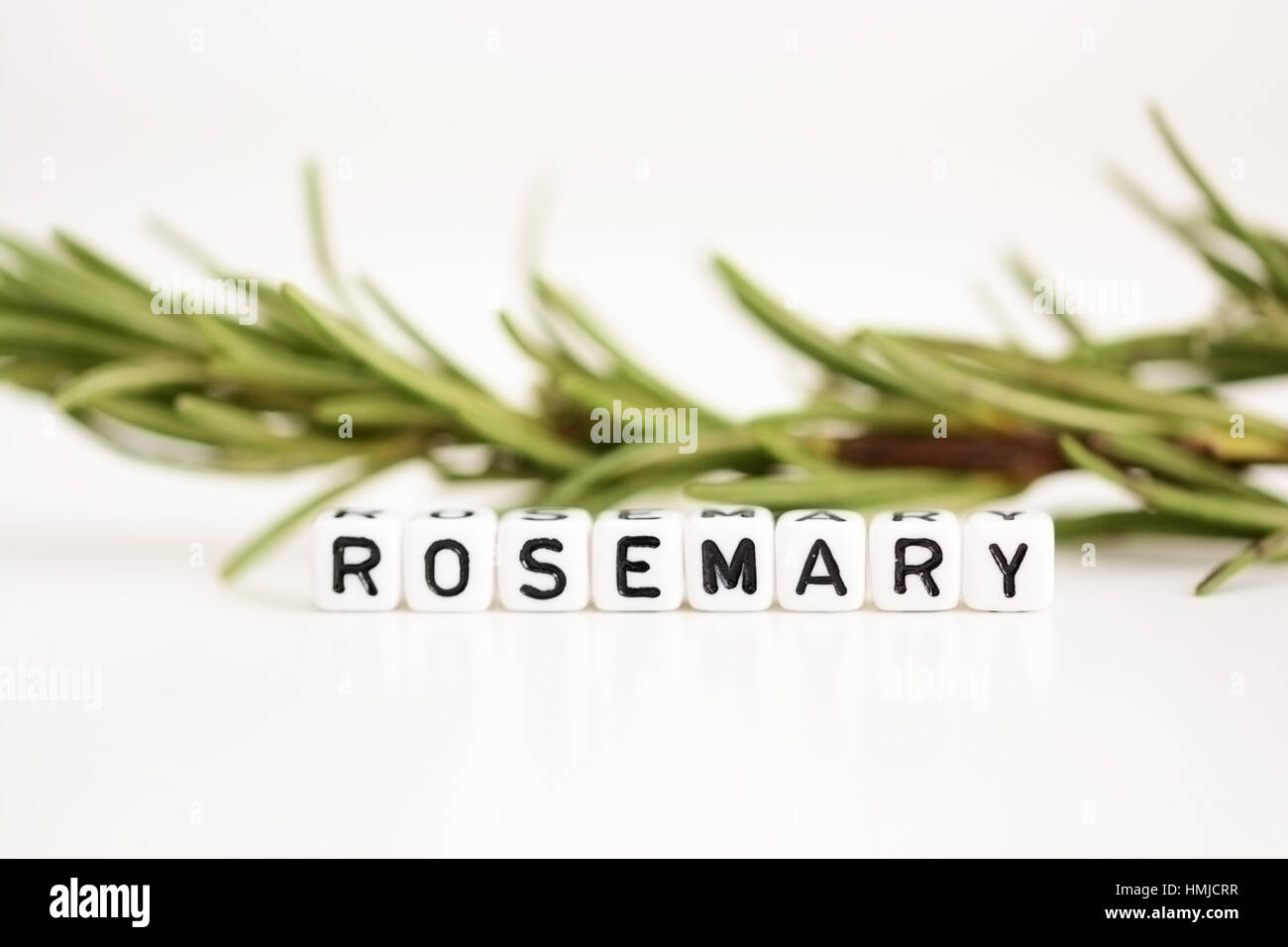 Blurred branch of rosemary in the background with close-up on plastic letter beads spelling “rosemary” Stock Photo