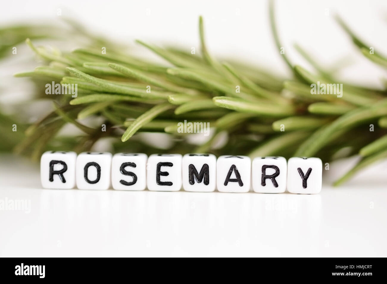 Blurred branch of rosemary in the background with close-up on plastic letter beads spelling “rosemary” Stock Photo