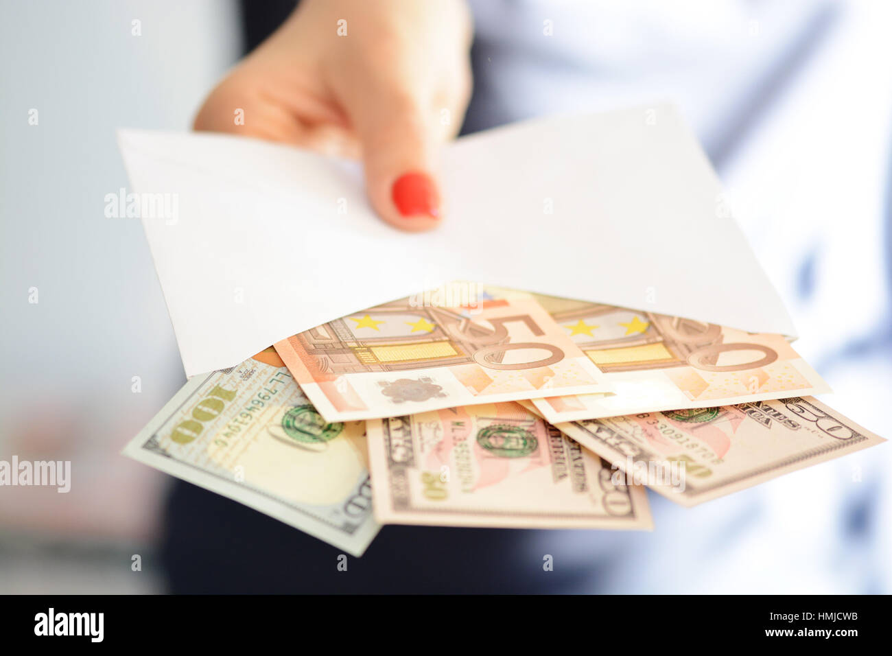 Woman handing out an envelope stuffed with euros and US dollar banknotes as bribe Stock Photo