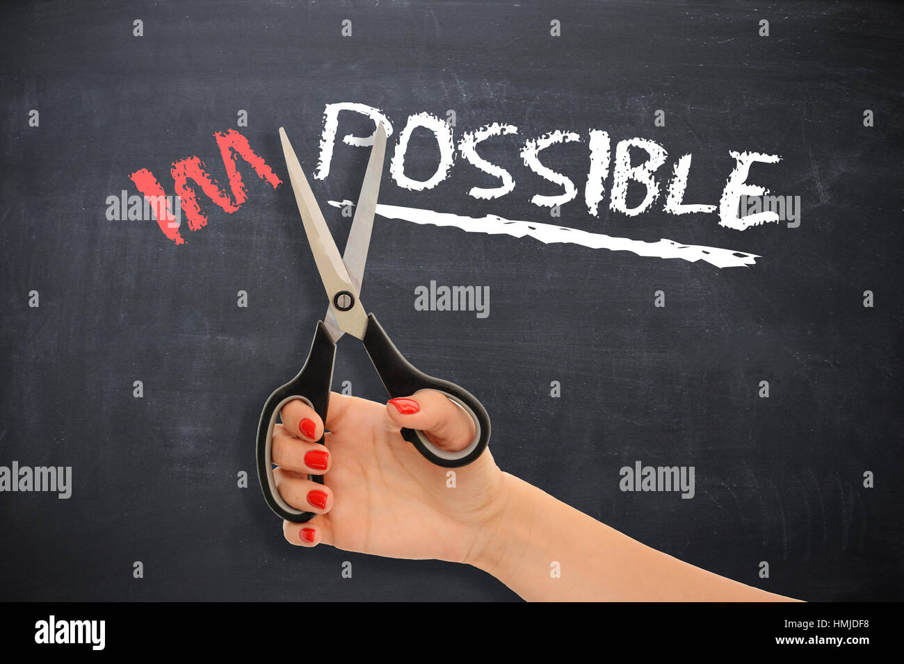 Motivational message on blackboard with woman cutting with scissors the word “impossible”, turning into the possible Stock Photo
