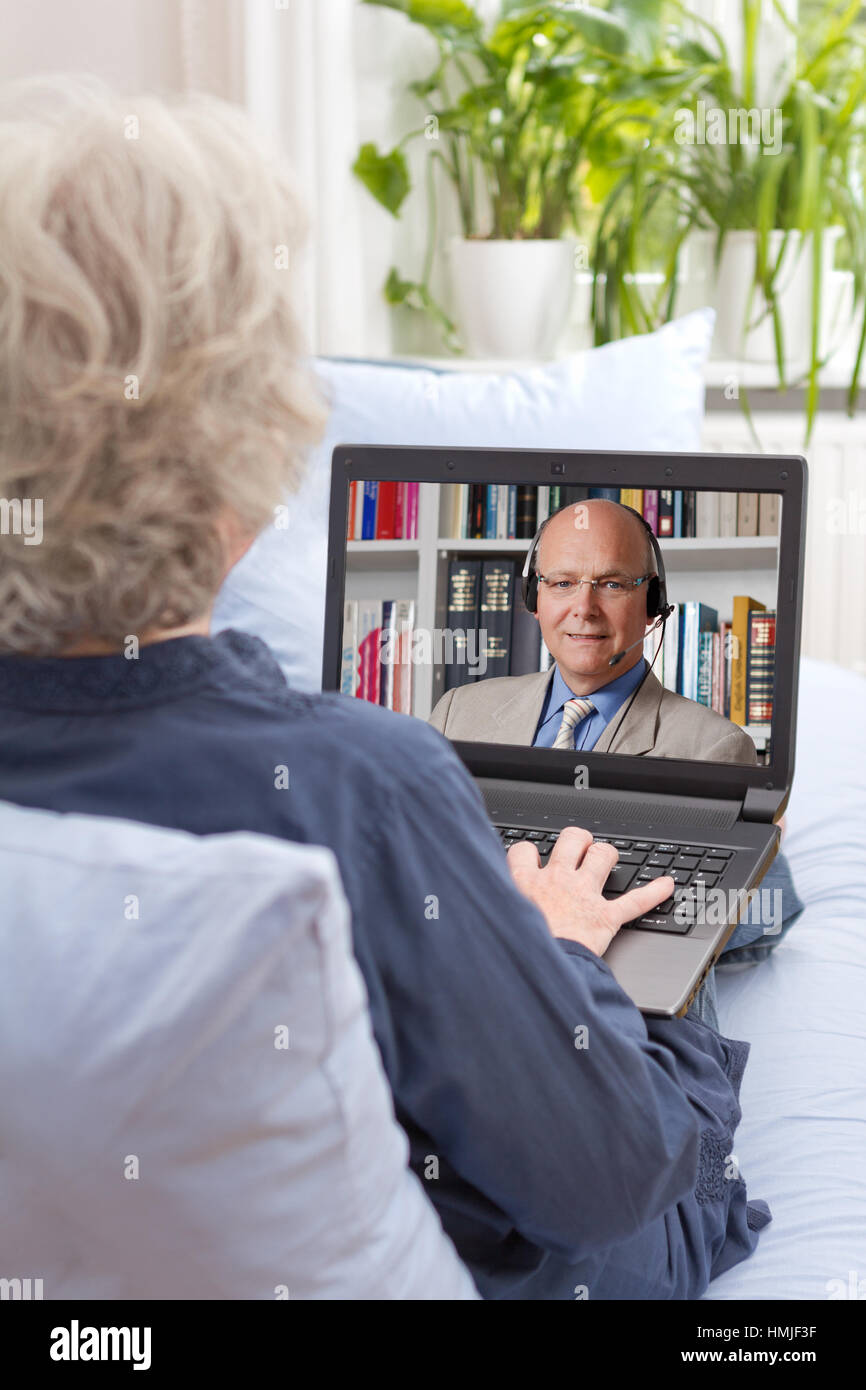 Rear view of a senior woman sitting relaxed with laptop on her couch, having an online live english lesson with her teacher, e-learning Stock Photo