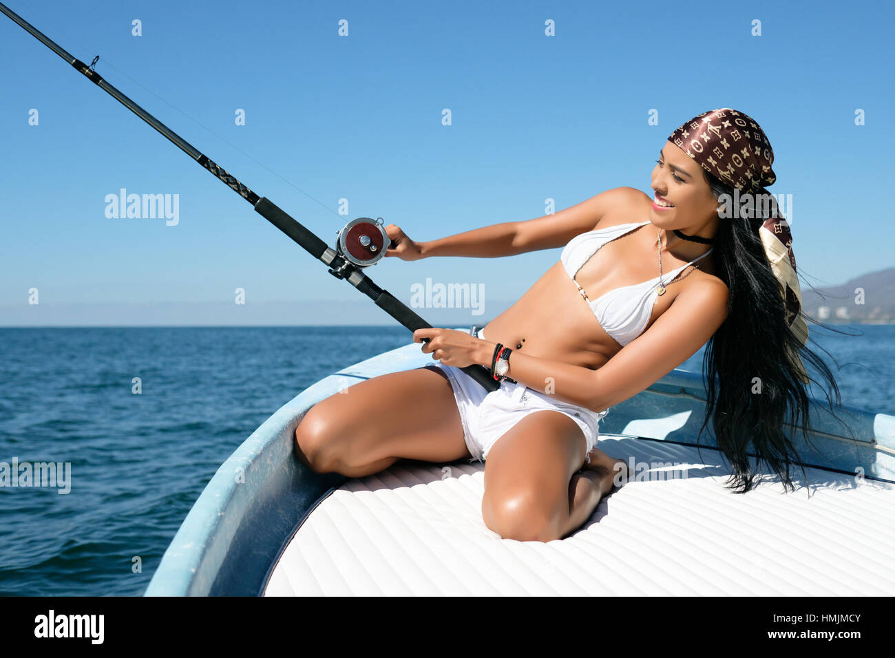 Attractive young hispanic woman leaning back while trying to reel in her catch at fishing off a boat. She looks happy and excited. Stock Photo