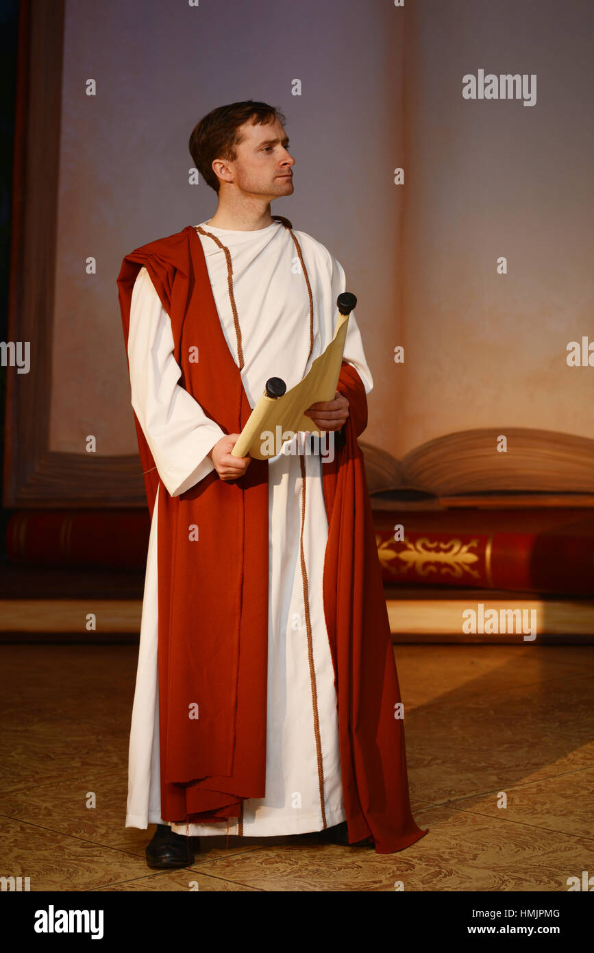 A character dressed in Roman costume reads from a scroll in front of a gigantic book Stock Photo