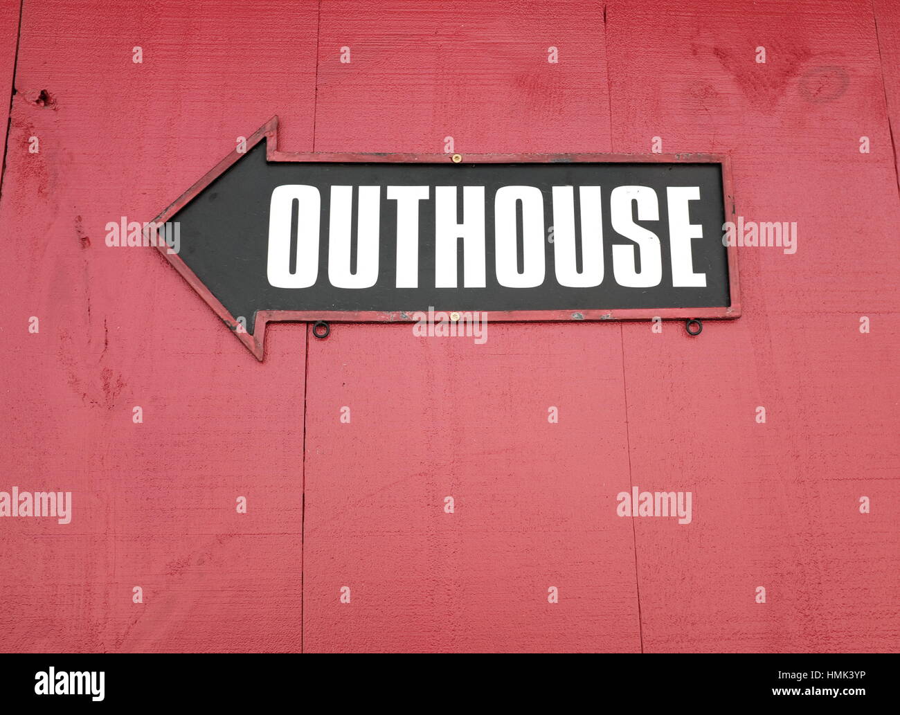 Sign pointing to outhouse on red wood Stock Photo