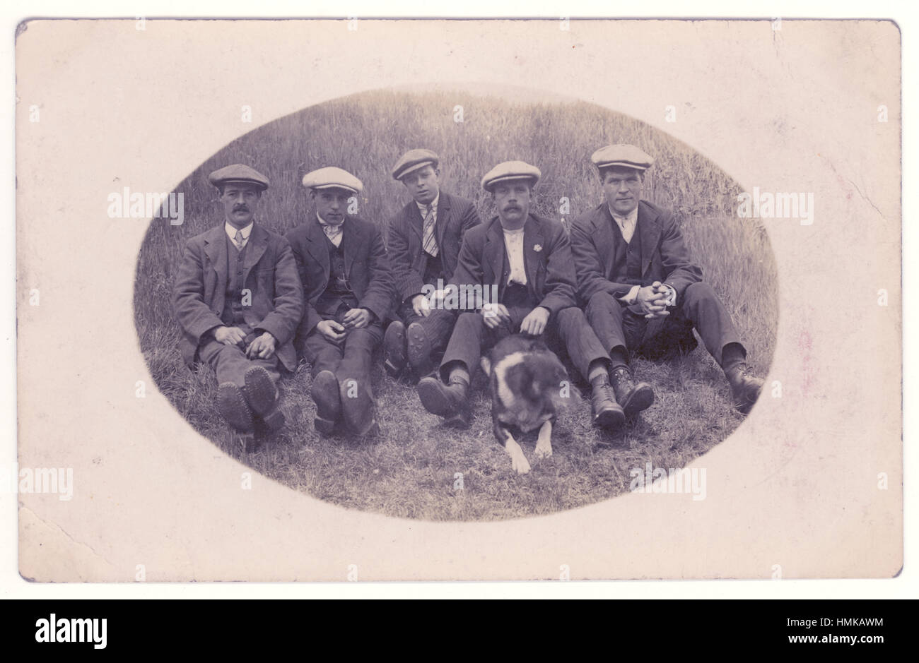 Early 1900's postcard of young working men characters and a dog in the countryside wearing flat caps and jackets possibly on a day trip. U.K. circa 1905 Stock Photo