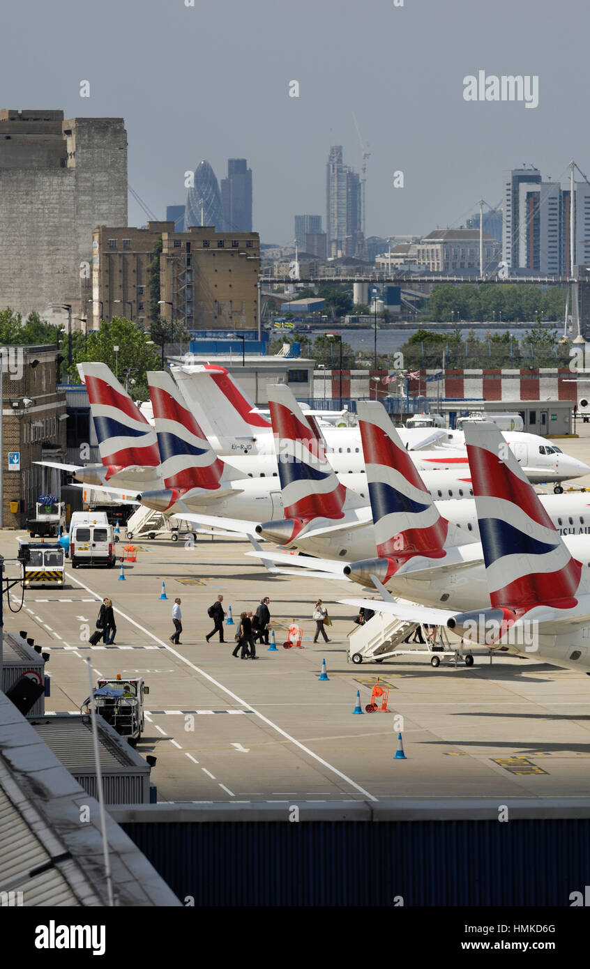tail-fins of British Airways BA CityFlyer Embraer 170s parked in a row at London City with skyscrapers behind Stock Photo