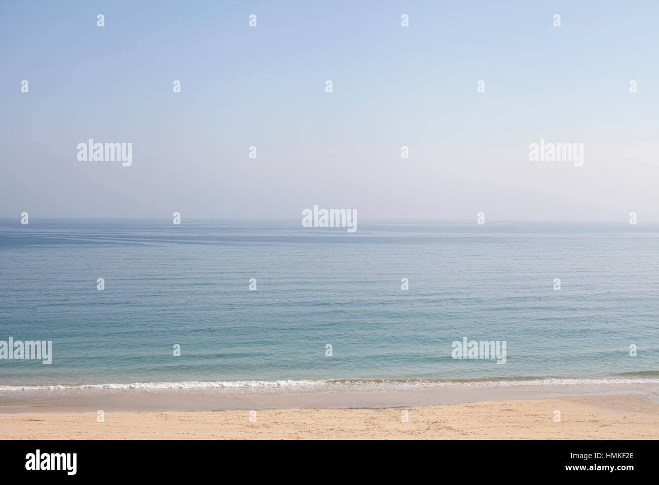 Calm sea and blue sky with small waves breaking on a sandy beach Stock Photo